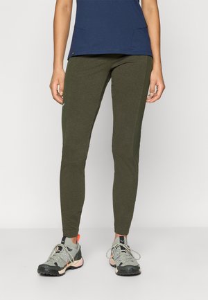 Zelené legíny vyrobené z elastického materiálu s priliehavým dizajnom a textúrovanými bočnými panelmi. Nosené s šedými outdoorovými topánkami s čiernymi akcentmi.