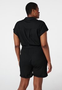 Zwarte short-sleeve jumpsuit met een kraag, textuurstof, een ceintuur in de taille en omgeslagen zoom, die een ontspannen pasvorm en detail met plooien op de rug toont.
