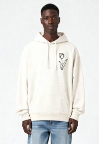 Sweat à capuche beige clair en tissu doux, avec un motif de tulipe noire sur la poitrine gauche et une poche avant. Coupe décontractée avec capuche à cordon.