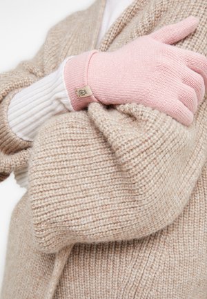 Knitted gloves in light pink, featuring ribbed cuffs. The hand is resting against a textured beige sweater, highlighting the soft materials.