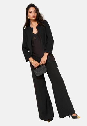 Black tailored blazer with long sleeves over a lace-trimmed top, paired with wide-leg trousers and heeled shoes, featuring a textured clutch.