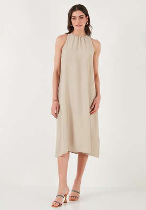 Beige sleeveless dress with a subtle texture, gathered neckline, and a flowing A-line silhouette, paired with multicolored heeled sandals.