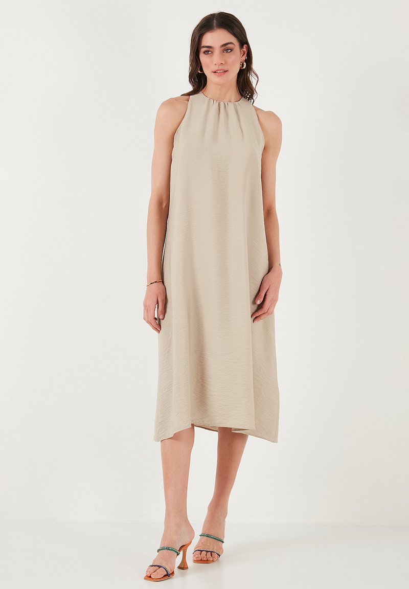 Beige sleeveless dress with a subtle texture, gathered neckline, and a flowing A-line silhouette, paired with multicolored heeled sandals.