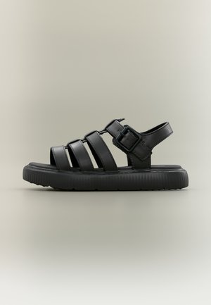 Sandale noire avec trois larges brides et une fermeture à boucle, dotée d'une semelle texturée et d'un design plat pour le confort et le maintien.
