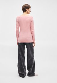 Dlhý rukáv, svetloružová blúzka s jemnou textúrou, okrúhlym výstrihom a priliehavým strihom, skombinovaná s širokými tmavosivými nohavicami.