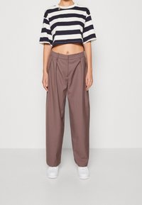 Krátký modro-bílý pruhovaný tričko s krátkým rukávem v kombinaci s béžovými kalhotami s vysokým pasem. Bílá sneakers dotváří outfit.