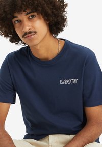 T-shirt de algodão azul-marinho com mangas curtas, apresentando um logótipo Levi's bordado em branco no peito. Textura suave e design clássico de decote redondo.