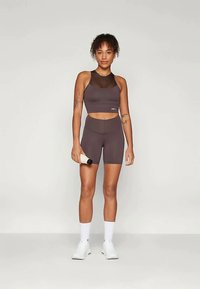 Σπορ σύνολο ενεργειακής ένδυσης σε σκούρο γκρι, περιλαμβάνοντας ένα κοντό τοπ με διχτυωτές επιφάνειες και σορτς με ψηλή μέση. Συμπεριλαμβάνεται μπουκάλι νερού και λευκά αθλητικά παπούτσια.