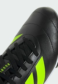 Scarpa da calcio nera in pelle con finitura texturizzata, dotata di accenti verde neon e lacci neri. Tre strisce diagonali sul lato.