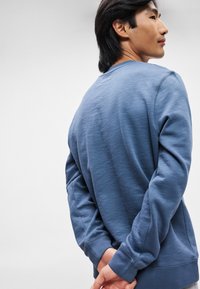 Sweatshirt azul de gola redonda com mangas longas, tecido texturizado e punhos canelados. Apresenta um corte relaxado e detalhes de costura flatlock.