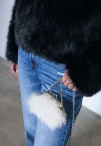 Sort faux fur top med en rund silhuet, parret med blå denim jeans. En lille hvid pels clutch med en sølv kæde holdes i hånden.