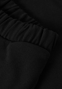 Tela negra con una textura suave, con detalles fruncidos en un lado. La composición parece blanda y cae fluidamente.