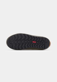 Suela de zapato con una banda de rodadura de goma negra que presenta surcos profundos y un acento naranja en el talón, diseñada para ofrecer tracción y durabilidad.