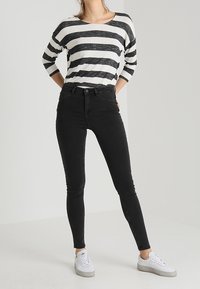 Musta kapea farkut yhdistettynä musta-valkoiseen raidalliseen pitkähihaiseen paitaan. Mallilla on yllään valkoiset lenkkarit; sileä kangas, muotoon ommeltu malli.