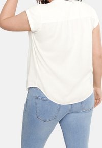 Woman wearing a loose white short-sleeve blouse and light blue jeans, shown from the back against a plain background.