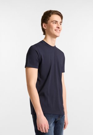  marineblauw T-shirt met korte mouwen van zachte katoen, met een ronde halslijn en een klein logo op de linkerborst. Draagt met blauwe spijkerbroek.
