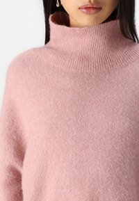Rosa Rollkragenpullover aus weichem, flauschigem Material mit geripptem Kragen und lockerer Passform. Verfügt über minimale Nähte und eine glatte Textur.