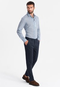Camicia a righe blu e bianche con bottoni abbinata a pantaloni navy. Le scarpe marroni completano l'outfit. La camicia presenta un colletto classico e maniche lunghe.