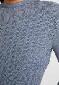 Maglione a maglia blu chiaro con texture a costine, caratterizzato da un motivo verticale di piccoli disegni a forma di foglia e un collo rotondo.