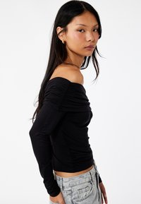 Top nero senza spalle con maniche lunghe, caratterizzato da una texture arricciata e un design aderente. Abbina a pantaloni corti in denim chiaro.