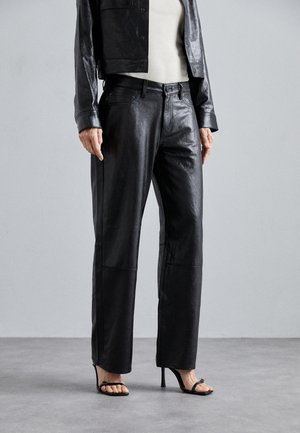 Crne kožne hlače s ravnim krojem i glatkim završetkom. Visok struk s bočnim džepovima i šivenim detaljima. Nosive s crnim remenastim potpeticama.