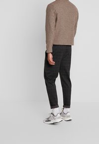 Ruskea ruutupuku, harmaat ruutuhousut ja harmaat lenkkitossut valkoisilla yksityiskohdilla. Kangas on kudottu ja siinä on hienovarainen tekstuuri sekä käänteet lahkeissa.