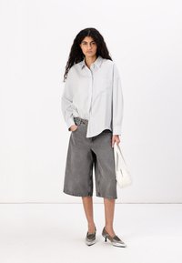 Camicia a righe grigia chiaro, taglio morbido, abbinata a pantaloni corti grigi scuri a gamba larga. Accessoriata con una borsa bianca e scarpe argentate lucide.