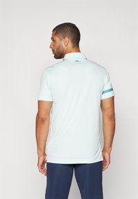 Himmelblaues Polohemd mit Kragen, kurzen Ärmeln und einem dezenten strukturierten Streifen am Ärmel. Verfügt über ein kleines Logo auf der Rückseite.