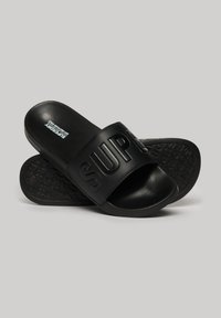 Svarte sandaler med bred rem, der har indgraveret "SUP" tekst, glat overflade og tekstureret gummisål med mønstre.