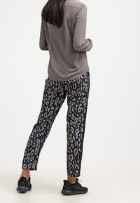 Grå langærmet top parret med løstsiddende sorte bukser med et multifarvet leopardmønster. Sorte sneakers fuldender outfittet.
