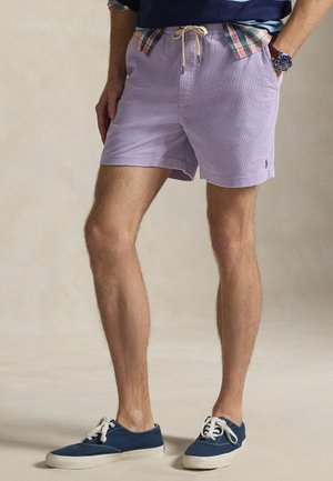 Μωβ ριγέ σορτς από ελαφρύ ύφασμα, με ελαστική μέση και κορδόνι, και πλαϊνές τσέπες. Συνδυασμένα με ναυτικό μπλε αθλητικά παπούτσια.