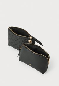 Dos bolsos negros con cremallera, uno con un patrón de logo texturizado y el otro liso, ambos con cremalleras y tiradores en tono dorado.