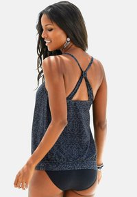 Top de tankini azul oscuro con un diseño estampado, tirantes ajustables y un lazo en la parte posterior. Combinado con un bañador negro. Tejido texturizado.