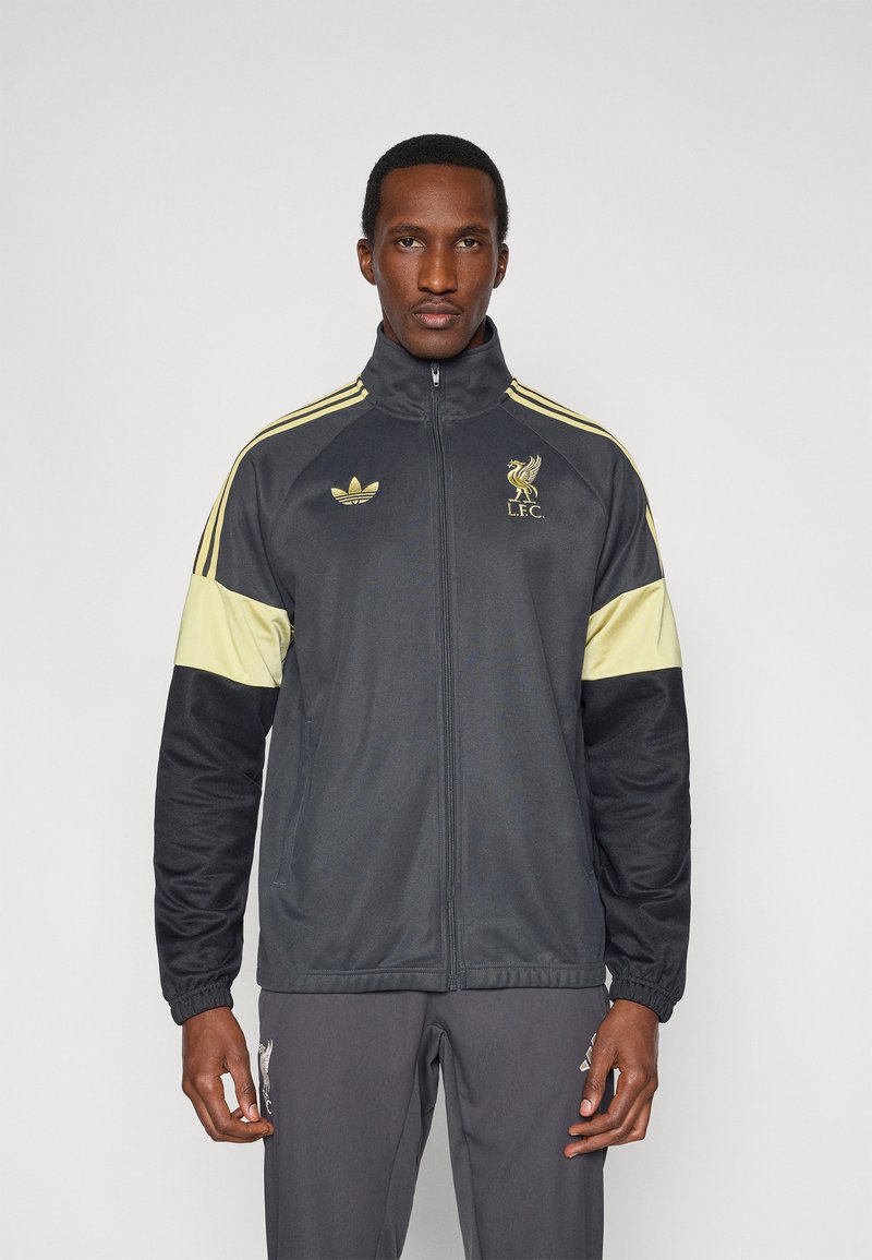 Čierno-žltá atletická bunda s vysokým golierom, obsahujúca logá Adidas a LFC, so zipsovým zapínaním a elastickými manžetami.