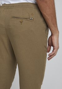 Pantalones marrones con una tela texturizada, cinturilla elástica y un bolsillo trasero abotonado que cuenta con un acento a rayas.