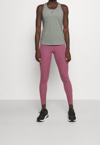 Top sportivo Nike in verde oliva, abbinato a leggings aderenti a vita alta in rosa chiaro. Scarpe sportive nere con accenti bianchi.