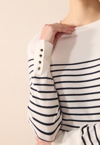 Pull en tricot avec des rayures bleu marine et blanches, orné de boutons dorés sur la manche. Matière douce, coupe décontractée et col rond.