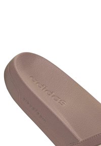 Adidas natikača u svijetloj mauve boji s teksturiranom gumiranom površinom, blago uočljivim lukom uložka i utisnutim markama i "cloudfoam" logotipima sa strane.
