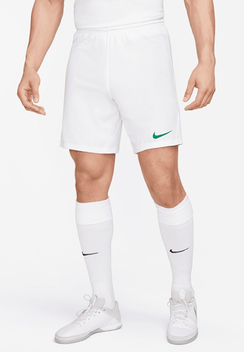 Shorts de sport blancs avec un swoosh Nike vert, associés à des chaussettes blanches montantes jusqu'au genou et des chaussures de sport gris clair, soulignant un look sportif.