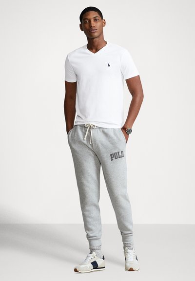 Biała bawełniana koszulka z dekoltem w serek oraz jasnoszare spodnie dresowe z wyhaftowanym napisem „POLO”. Codzienne buty sportowe z granatowymi i kremowymi akcentami.