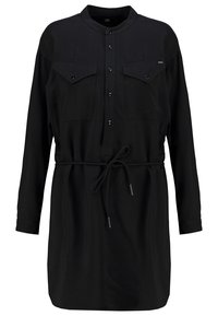 Vestido negro de camisa con mangas largas, cierre frontal de botones, dos bolsillos en el pecho y cintura con cordón. Hecho de tejido ligero.