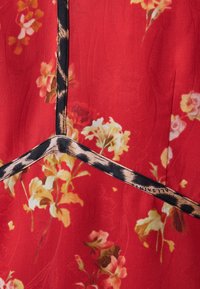 Tissu rouge à imprimé floral avec bordure noire à motif léopard se croisant en forme de V.
