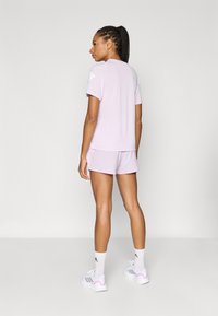 Gaiši lavandas sporta krekls ar īsām piedurknēm, kopā ar atbilstošiem šortiem. Audums izskatās gluds. Baltas sporta kurpes ar rozā akcentiem.