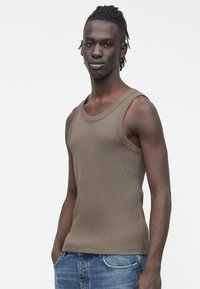 Bruine geribbelde tanktop met brede schouderbanden, strakke pasvorm, contrasterende textuur, gecombineerd met blauwe spijkerbroek.