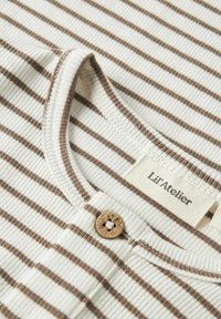 Koszula bawełniana w paski o wąskich brązowych i kremowych liniach, z zaokrąglonym kołnierzykiem, drewnianym guzikiem oraz metką z napisem "Lil'Atelier".