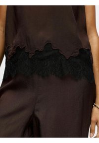 Top senza maniche marrone con orlo scallop e rifiniture in pizzo nero. Tessuto liscio con un leggero lucido e dettagli in pizzo delicato sul fondo.