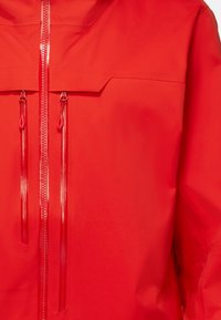 Rote wasserdichte Jacke mit hohem Kragen, Reißverschluss vorne mit zwei Ziehlaschen und glatter, matter Oberfläche. Leichtes, elegantes Design.