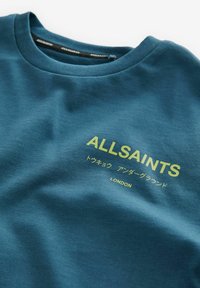 Teal bomulds t-shirt med rund hals, med gult tekst "ALLSAINTS" og yderligere japanske tegn trykt på forsiden.