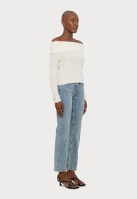 Off-white rebrast top z odprti rameni, svetlo modri naravnost krojeni kavbojke, črne sandale z naramnicami. Minimalističen dizajn z sproščenim krojem, brez vzorcev.