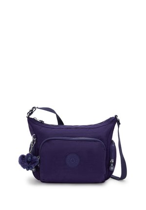 Lilla crossbody taske med lynlås foran, justerbar strop og lille plysch nøglering hængende ved lynlåsen.
